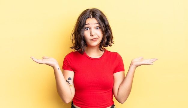 Jeune jolie fille se sentant perplexe et confuse, doutant, pondérant ou choisissant différentes options avec une expression amusante