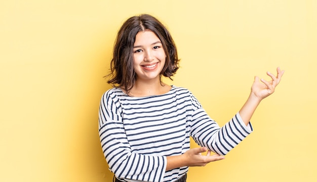 Jeune jolie fille souriant fièrement et en toute confiance se sentant heureuse et satisfaite et montrant un concept sur l'espace de copie