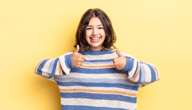 Jeune jolie fille souriante ayant l'air heureuse, positive, confiante et réussie, avec les deux pouces vers le haut