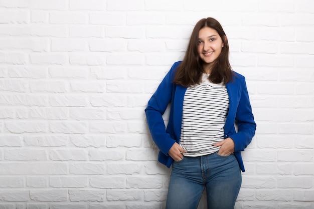 Une jeune jolie fille souriante contre un mur de briques de style loft blanc Elle regarde le spectateur Copier l'espace