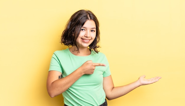 jeune jolie fille souriante, se sentant heureuse, insouciante et satisfaite, pointant vers le concept ou l'idée sur l'espace de copie sur le côté