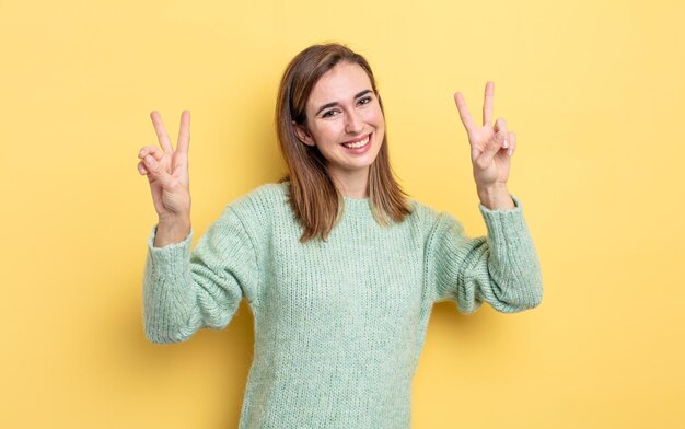 Jeune jolie fille souriante et semblant heureuse, amicale et satisfaite, gesticulant la victoire ou la paix avec les deux mains