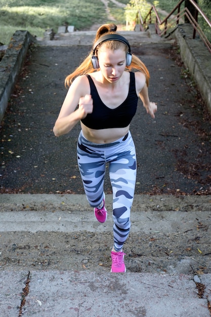 Jeune jolie fille sportive joyeuse monte les escaliers et écoute de la musique.