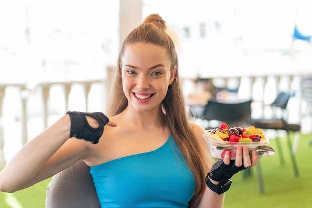 Jeune jolie fille sportive tenant un bol de fruits à l'extérieur avec une expression faciale surprise