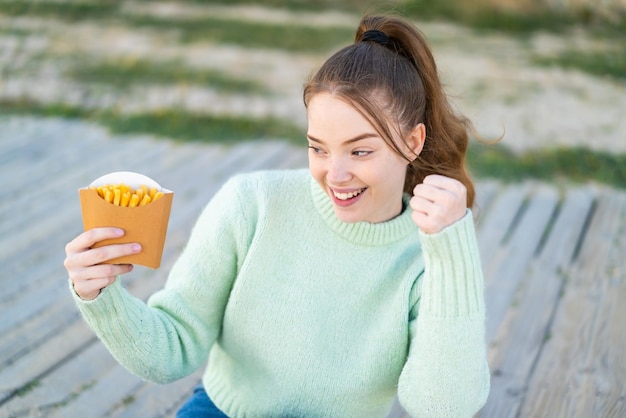 Jeune Jolie Fille Tenant Des Frites Frites à L'extérieur Célébrant Une Victoire