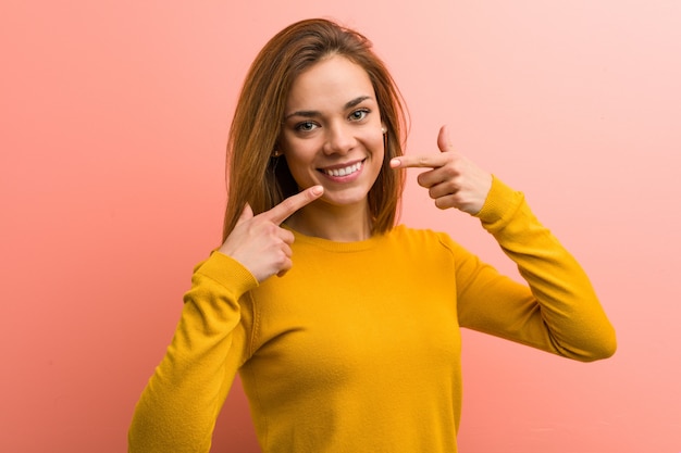 Jeune et jolie jeune femme sourit et pointe ses doigts vers la bouche.