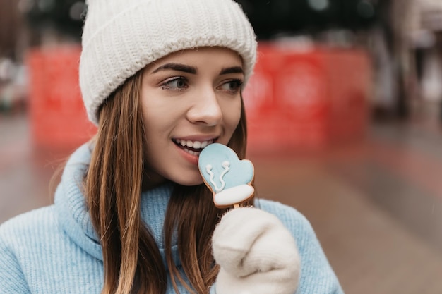 Jeune jolie jolie femme debout dans la rue mangeant des biscuits au chocolat aux bonbons au pain d'épice sur un bâton