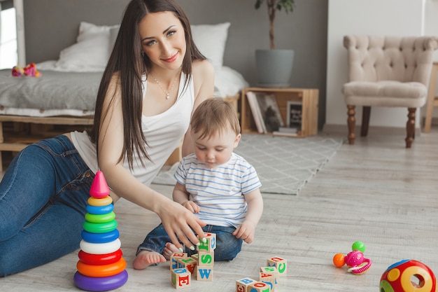 Jeune jolie mère jouant avec son petit fils. Famille joyeuse s'amuser à l'intérieur avec petit bébé