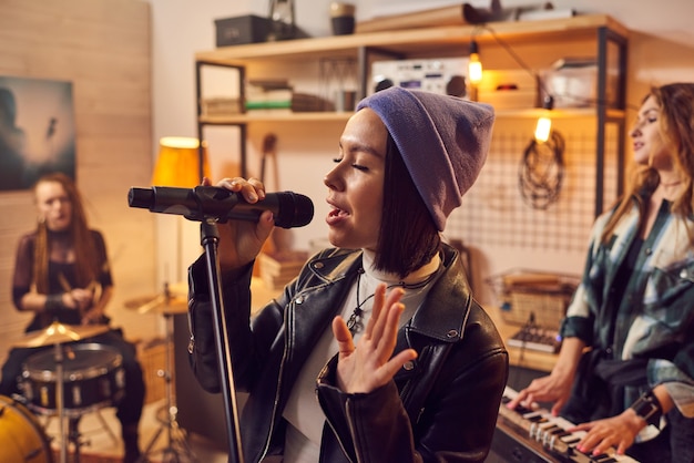 Jeune jolie musicienne enregistrant des chansons avec un groupe en studio