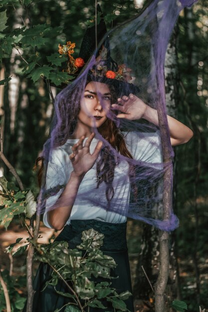 Jeune jolie sorcière au chapeau noir se bouchent dans la forêt. Whitch cosplay d'halloween. Traitement de l'art.