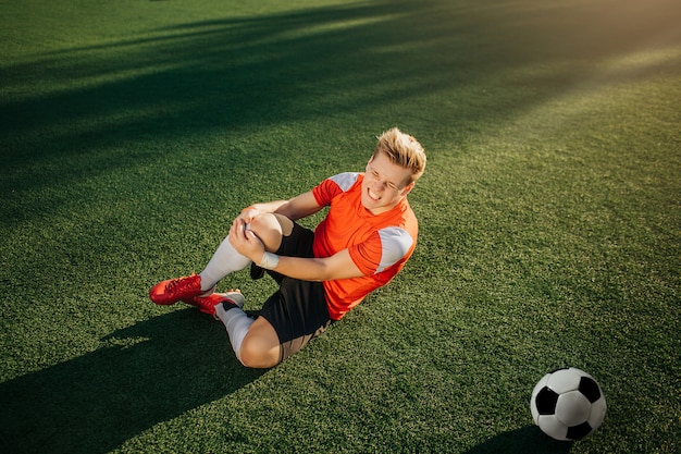 Jeune joueur de football allongé sur la pelouse verte et tenir la main autour de la jambe. Il a eu un traumatisme. Guy ressent une douleur terrible. Il souffre.