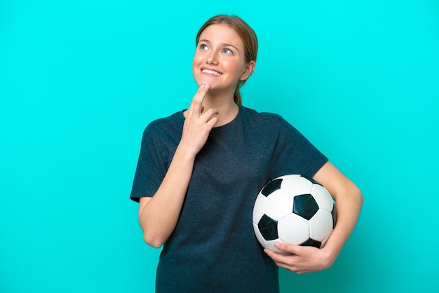 Jeune joueur de football femme isolée sur fond bleu levant les yeux en souriant