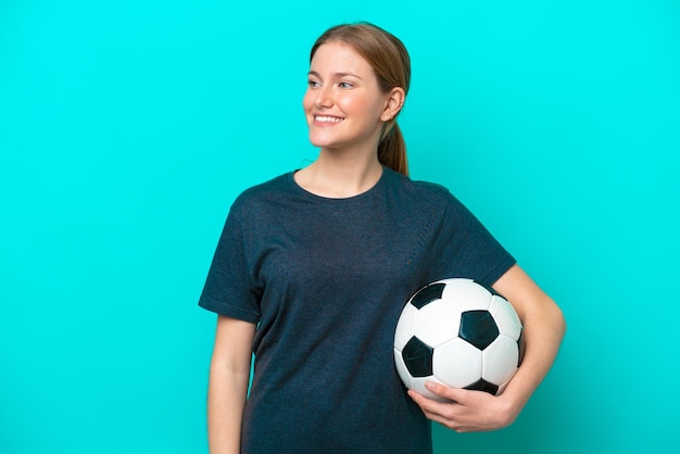 Jeune joueur de football femme isolée sur fond bleu regardant sur le côté et souriant