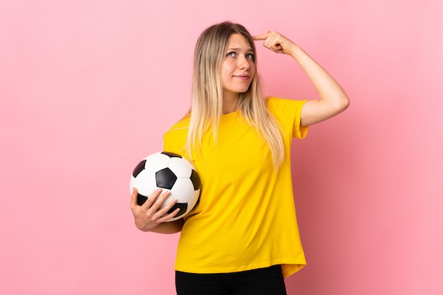 Jeune joueur de football femme isolée sur un mur rose ayant des doutes avec une expression de visage confuse