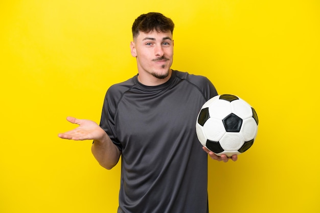 Jeune joueur de football homme isolé sur fond jaune ayant des doutes tout en levant les mains