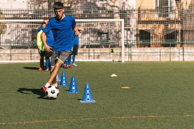 Jeune joueur gaucher dribble les cônes avec un ballon de football