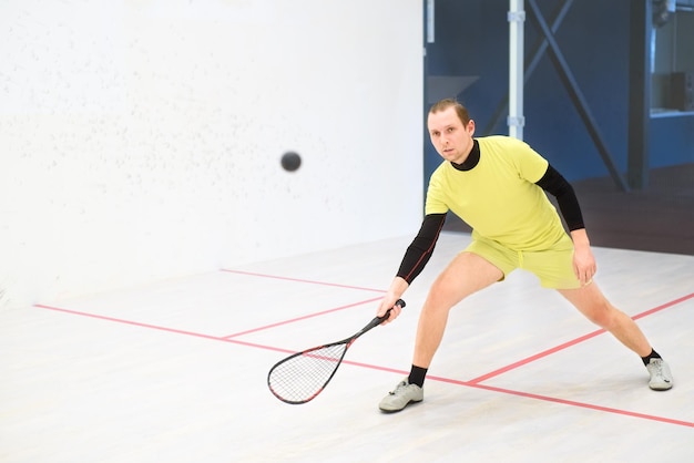 jeune joueur de squash caucasien frappant une balle dans un court de squash