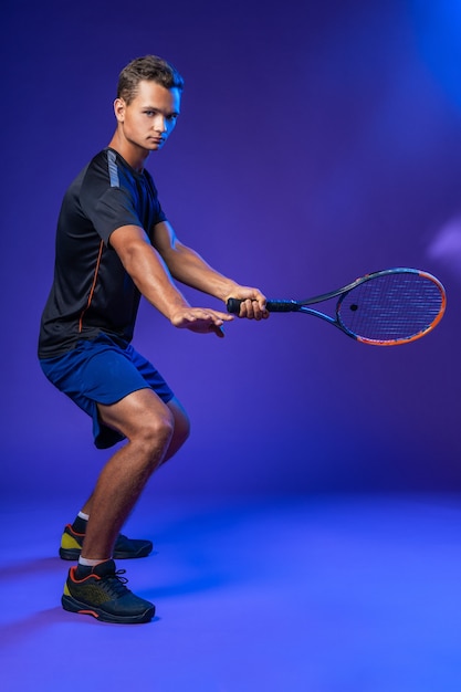 Jeune joueur de tennis en action sur fond violet, portrait en pied