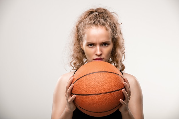 Jeune joueuse de basket-ball tenant le ballon par son visage en se tenant debout et en regardant son rival sur le gris