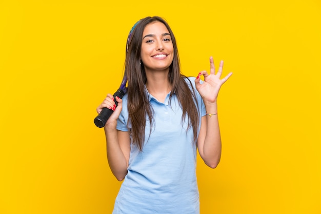 Jeune joueuse de tennis isolée sur un mur jaune montrant un signe ok avec les doigts