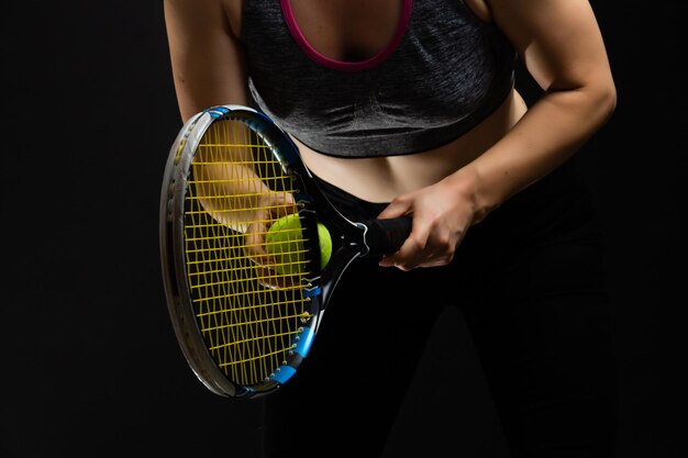 Jeune joueuse de tennis posant avec une raquette sur fond noir