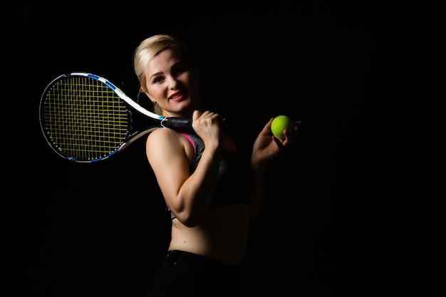 Jeune joueuse de tennis posant avec une raquette sur fond noir