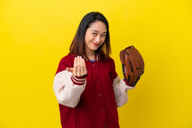 Jeune joueuse vietnamienne avec gant de baseball isolé sur fond jaune invitant à venir avec la main. Heureux que tu sois venu