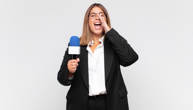 Jeune journaliste se sentant heureuse, excitée et positive, donnant un grand cri avec les mains à côté de la bouche, appelant