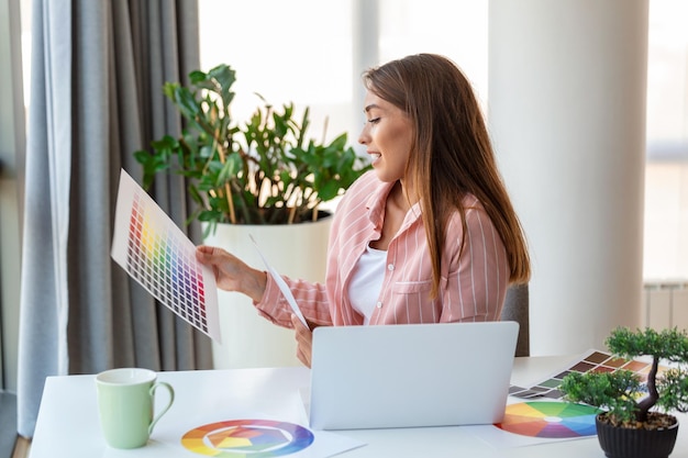 Une jeune et joyeuse femme designer ayant une vidéoconférence avec des clients assis à leur bureau devant l'ordinateur tenant des palettes de couleurs faisant des gestes et souriant dans l'espace de copie