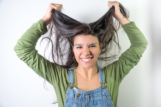 Jeune latina souriante tirant les cheveux coiffeur à la maison cheveux très longs sur fond neutre