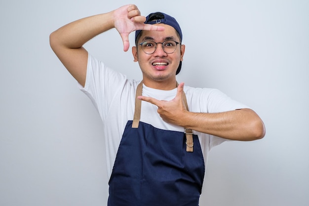 Jeune livreur asiatique portant des lunettes et une casquette souriant faisant un cadre avec les mains et les doigts avec un visage heureux