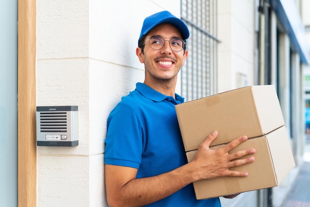 Jeune livreur à l'extérieur tenant des boîtes avec une expression heureuse