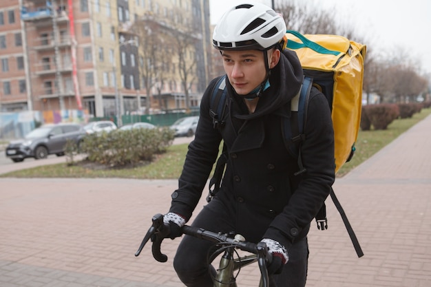 Jeune livreur portant sac à dos thermo, cyclisme dans les rues de la ville en automne