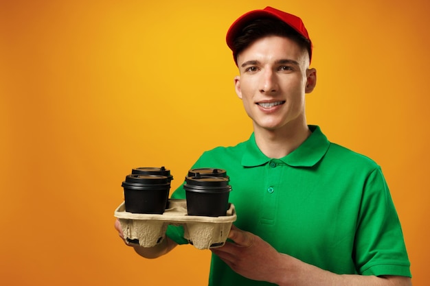 Jeune livreur tenant des tasses à café sur fond jaune