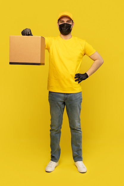 Jeune livreur en tshirt jaune, masque, gants avec boîte isolé