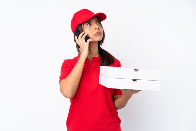 Jeune livreuse de pizza sur mur blanc isolé tenant du café à emporter et un mobile