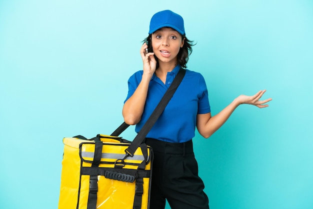 Jeune livreuse avec sac à dos thermique gardant une conversation avec le téléphone portable avec quelqu'un