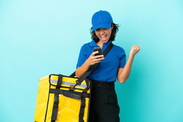 Jeune livreuse avec sac à dos thermique avec téléphone en position de victoire