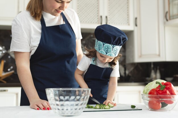 Jeune maman et adorable petite fille mignonne portant un tablier, hacher des légumes