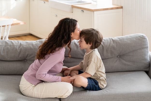 Jeune maman aimante embrassant l'enfant dans la relation tendre du front entre le parent et l'enfant d'âge préscolaire