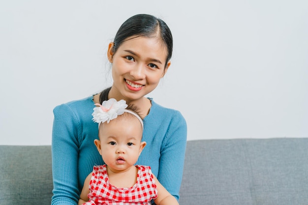 Jeune maman asiatique avec une jolie petite fille assise sur un canapé ensemble dans le salon