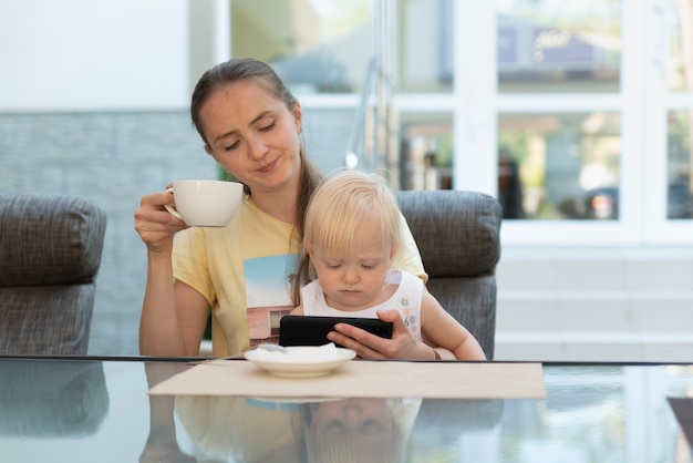 Jeune maman au café avec enfant dans ses bras boit du café et regarde le téléphone. Maman d'affaires moderne.