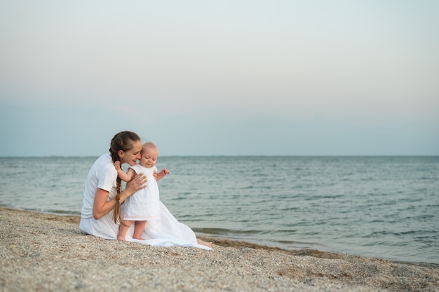 Jeune maman et bébé assis sur une plage de sable. Vacances à la mer avec de petits enfants