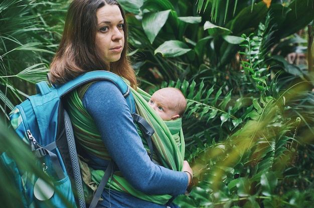 Une jeune maman avec un bébé en écharpe marche dans la jungle