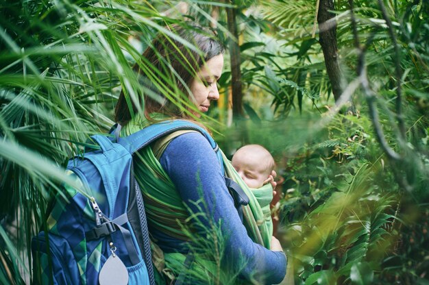 Une jeune maman avec un bébé en écharpe marche dans la jungle