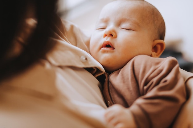 Jeune maman brune et son nouveau-né dans ses bras photo à la maison dans une pièce sombre près de la fenêtre