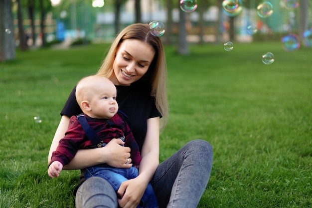 Jeune maman caucasienne gonfle des bulles de savon avec son petit fils dans un parc par une journée d'été ensoleillée.