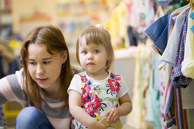 Jeune maman caucasienne avec sa fille au magasin de vêtements pour enfants