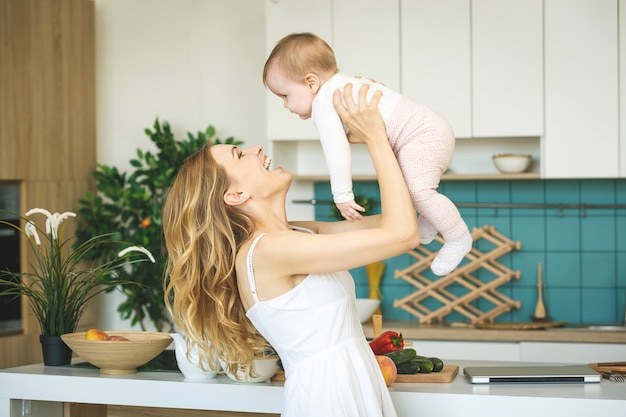 Jeune maman cuisine et joue avec sa petite fille dans une cuisine moderne.