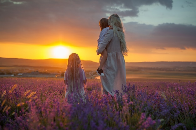 Une jeune maman avec deux enfants regardant le soleil sortant dans un champ de lavande